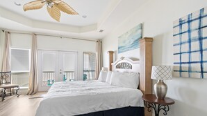 Un dormitorio con cama, ventilador de techo, mesita de noche, lámpara y vistas al balcón.
