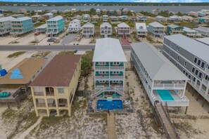 Una zona residencial costera con propiedades frente al mar, incluyendo un edificio de dos plantas con piscina y un edificio independiente con una gran piscina.