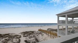 Vista de la playa con un paseo de madera que conduce a un edificio blanco con balcón.