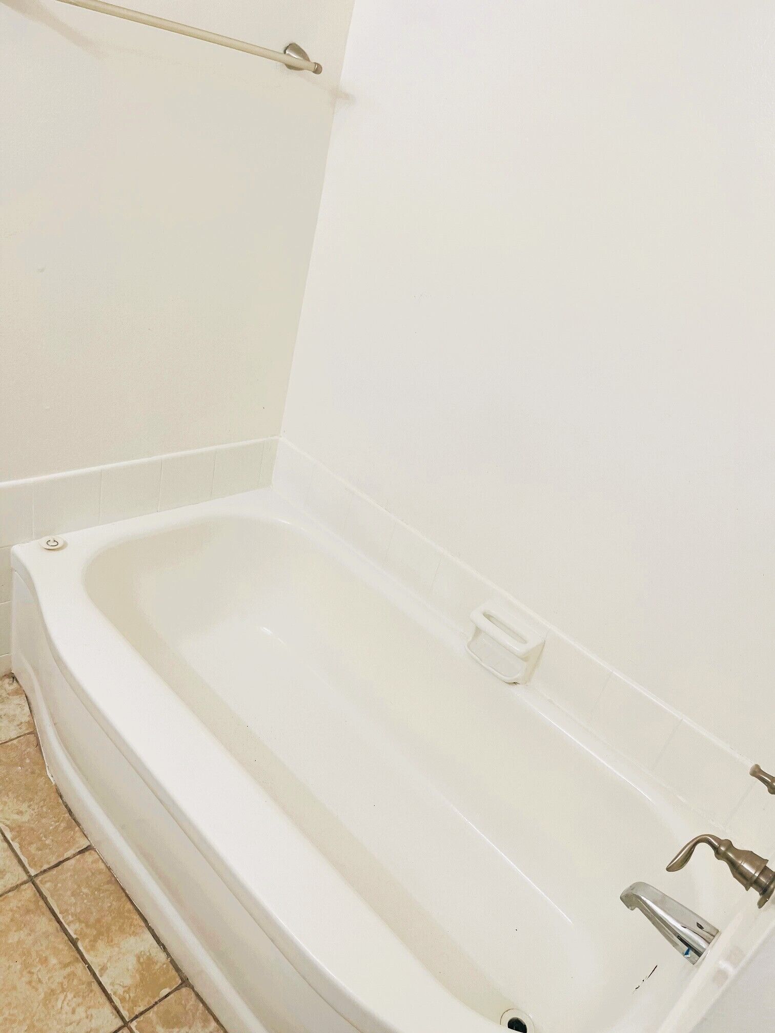 Una bañera blanca con grifo, jabonera, toallero y suelo de baldosas.