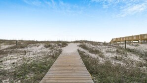 A wooden boardwalk leading to a wooden structure with a railing, surrounded by sand dunes and sparse vegetation.