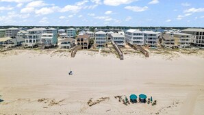 A beachfront hotel with multiple-story buildings, a sandy beach, and a wooden boardwalk leading to the water.