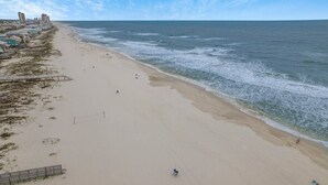 Une plage avec un rivage sablonneux, quelques personnes et des bâtiments en arrière-plan.