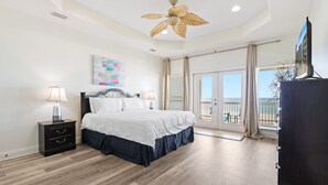 Een slaapkamer met een bed, nachtkastjes, een plafondventilator, een schilderij en een balkon met uitzicht.