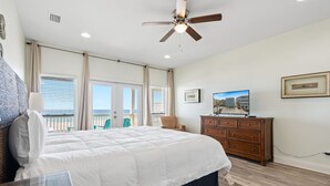 Een slaapkamer met een bed, een dressoir, een plafondventilator, een raam en een balkon.