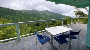 A balcony with a table and chairs overlooking a mountainous landscape. - Perfect for large groups - House & Triplex w/private river access (Naguabo)