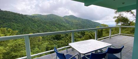 A balcony with a table and chairs overlooking a mountainous landscape.