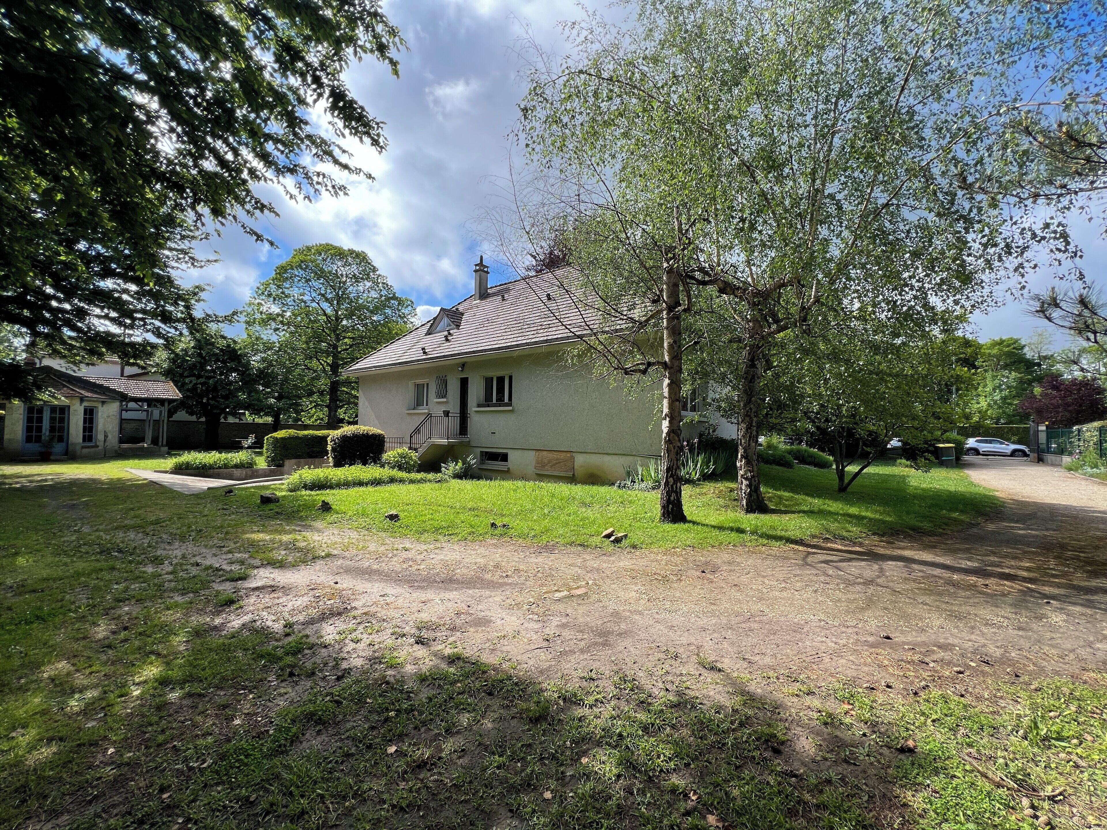 Ein zweistöckiges Haus mit einer Veranda, einem kleinen Garten und einem gepflasterten Einfahrtsweg.