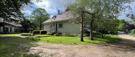 A two-story house with a front porch, a small garden, and a paved driveway.