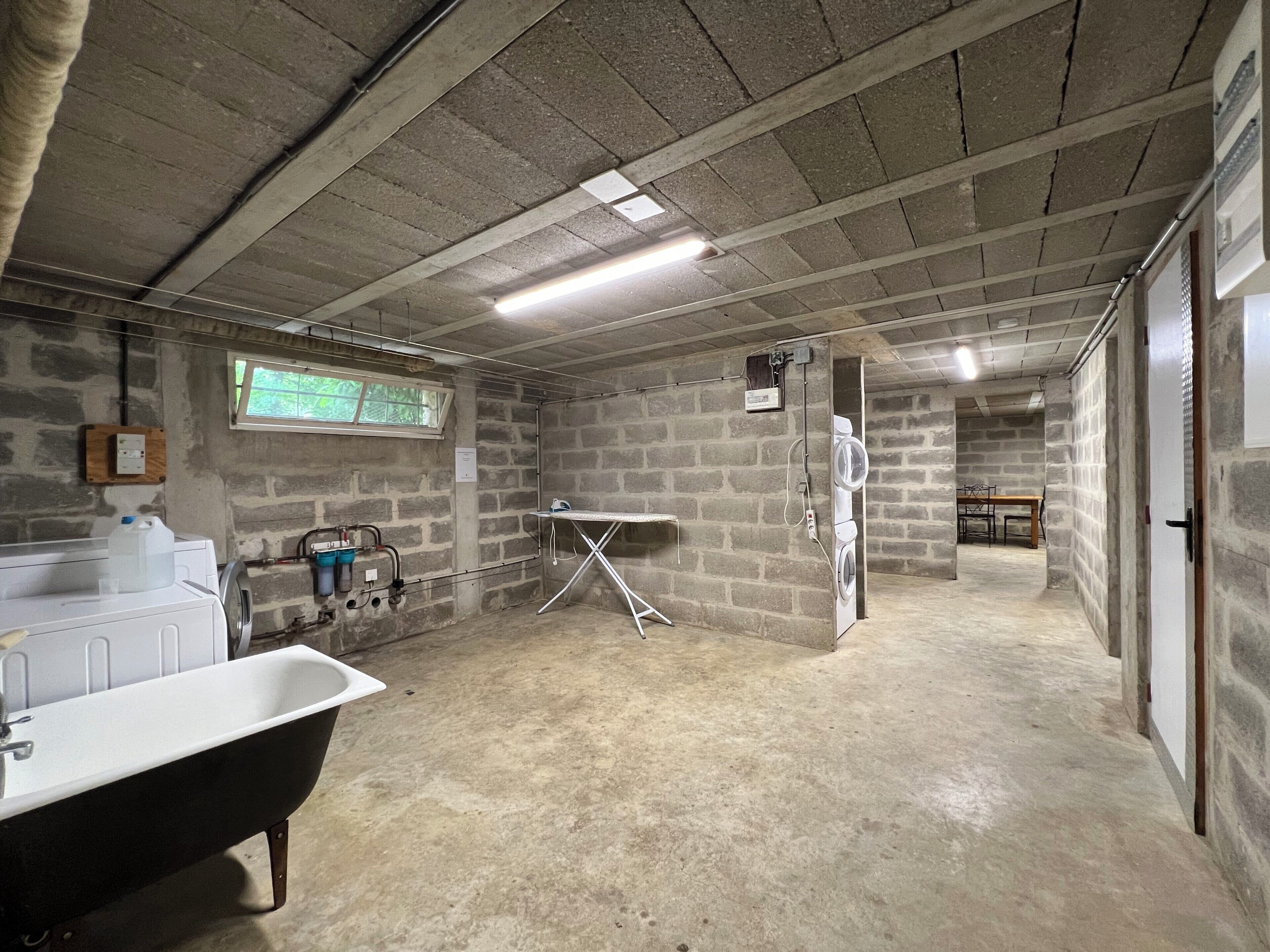 Ein Kellerraum mit einer großen Badewanne, einer Waschgelegenheit und einem Fenster mit Blick auf Grünflächen.