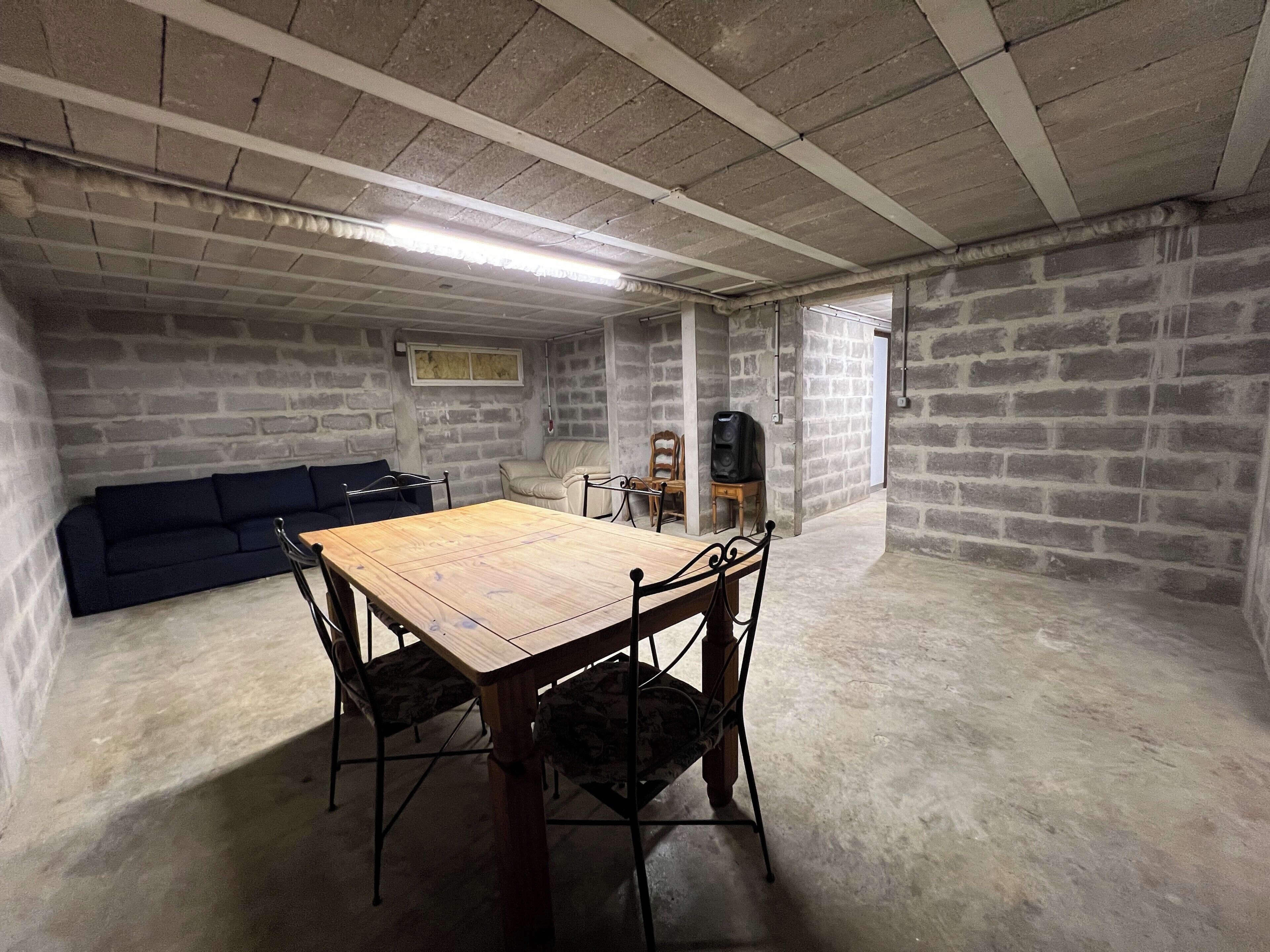A basement with a wooden table and chairs, a blue sofa, and a stone wall.