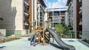 Un espace de jeux extérieur doté d’un toboggan et d’une structure d’escalade, entouré d’immeubles modernes.
