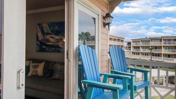 Een balkon met twee blauwe Adirondack-stoelen, een schilderij aan de muur en uitzicht op andere gebouwen.
