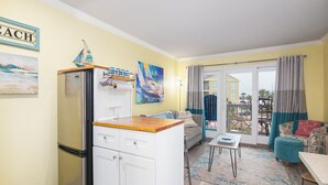 Een ruimtelijk ingerichte leefruimte met een kitchenette, een bank, een tafeltje en een balkon met gordijnen.