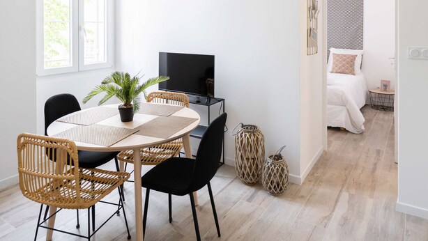 Een moderne, goed verlichte kamer met een eethoek, een televisie en een bed in de aangrenzende kamer.