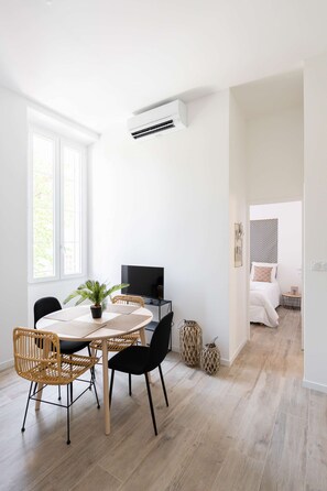 Una habitación moderna y bien iluminada con comedor, televisor y cama en la habitación contigua.
