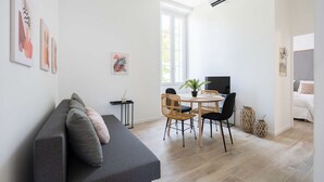 Een moderne woonkamer met een grijze bank, een eettafel met rieten stoelen en een flatscreen televisie.