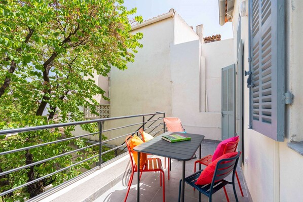 An outdoor balcony with a table and chairs, a railing, and a tree.