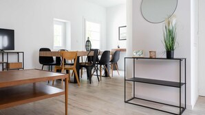 A modern living room with a wooden dining table, black chairs, a TV on a stand, and a large mirror on the wall. - Maisonmars Le Concorde 3 (Marseille)