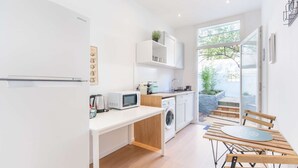 A modern kitchen with white cabinetry, a microwave, a kettle, and a washing machine. There is a dining area with a wooden table and chairs. - Maisonmars Le Complexe Blancarde (Marseille)