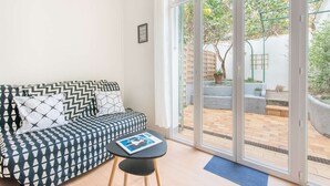 A modern living room with a patterned sofa, a small round table, and a large sliding glass door leading to an outdoor patio area. - Maisonmars Le Complexe Blancarde (Marseille)