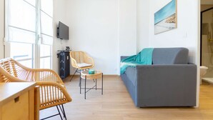 Un salon moderne avec un canapé gris, des fauteuils en osier, une petite table et un téléviseur.