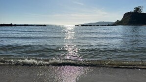 A beach with calm waters reflecting sunlight, a sandy shore, and a distant rocky coastline. - The terrace by the sea (Sciacca)