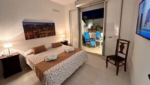 A hotel room with a bed, a nightstand, a lamp, a painting, a chair, and a balcony with chairs and a table. - The terrace by the sea (Sciacca)