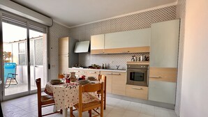 A modern kitchen with a dining area, featuring a table set for four, a stove, oven, and a sink. - The terrace by the sea (Sciacca)