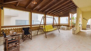 Ein überdachter Patio-Bereich mit Schaukel, Holzstühlen und einem Tisch mit Bank.