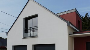 Una casa moderna de dos pisos con garaje, balcón y puerta roja.