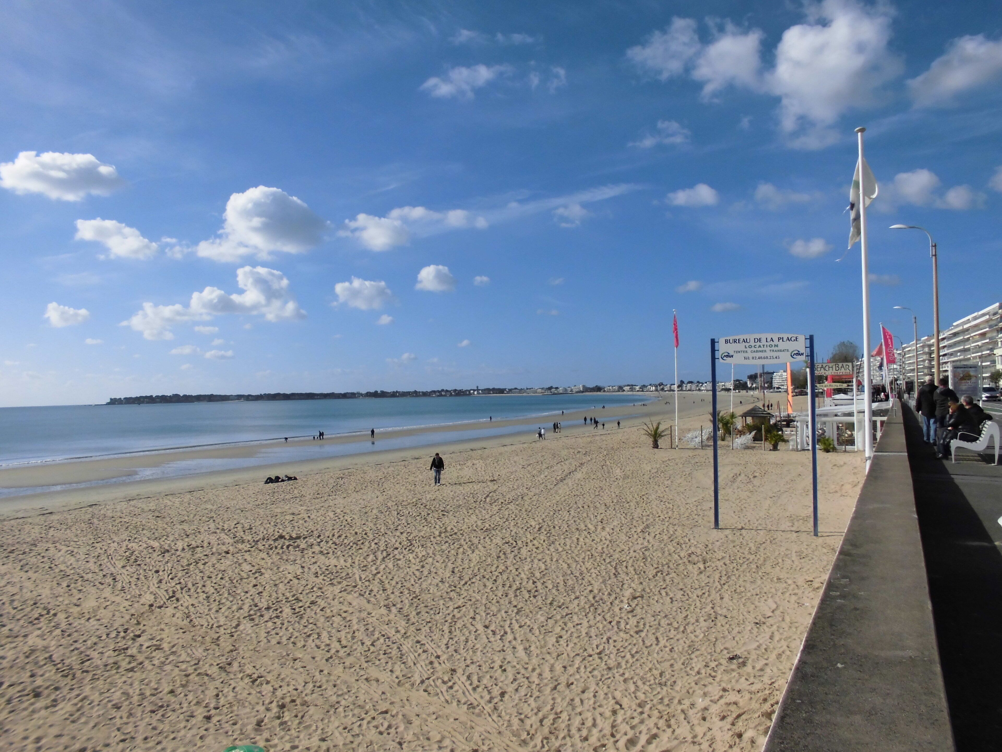 A beach with a promenade, flags, and a signboard.