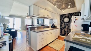 A modern kitchen with a central island, white cabinetry, and a decorative wall clock. - 3 Bedroom Condo on the beach. (Murrells Inlet)