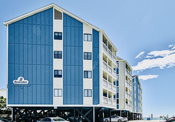 Ein mehrstöckiges Hotel mit blau-weißer Fassade, einem Schild mit der Aufschrift "Seasider" und einem Parkplatz davor.