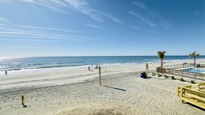 Ein Strand mit einer Holzterrasse, einem Pool und Palmen.