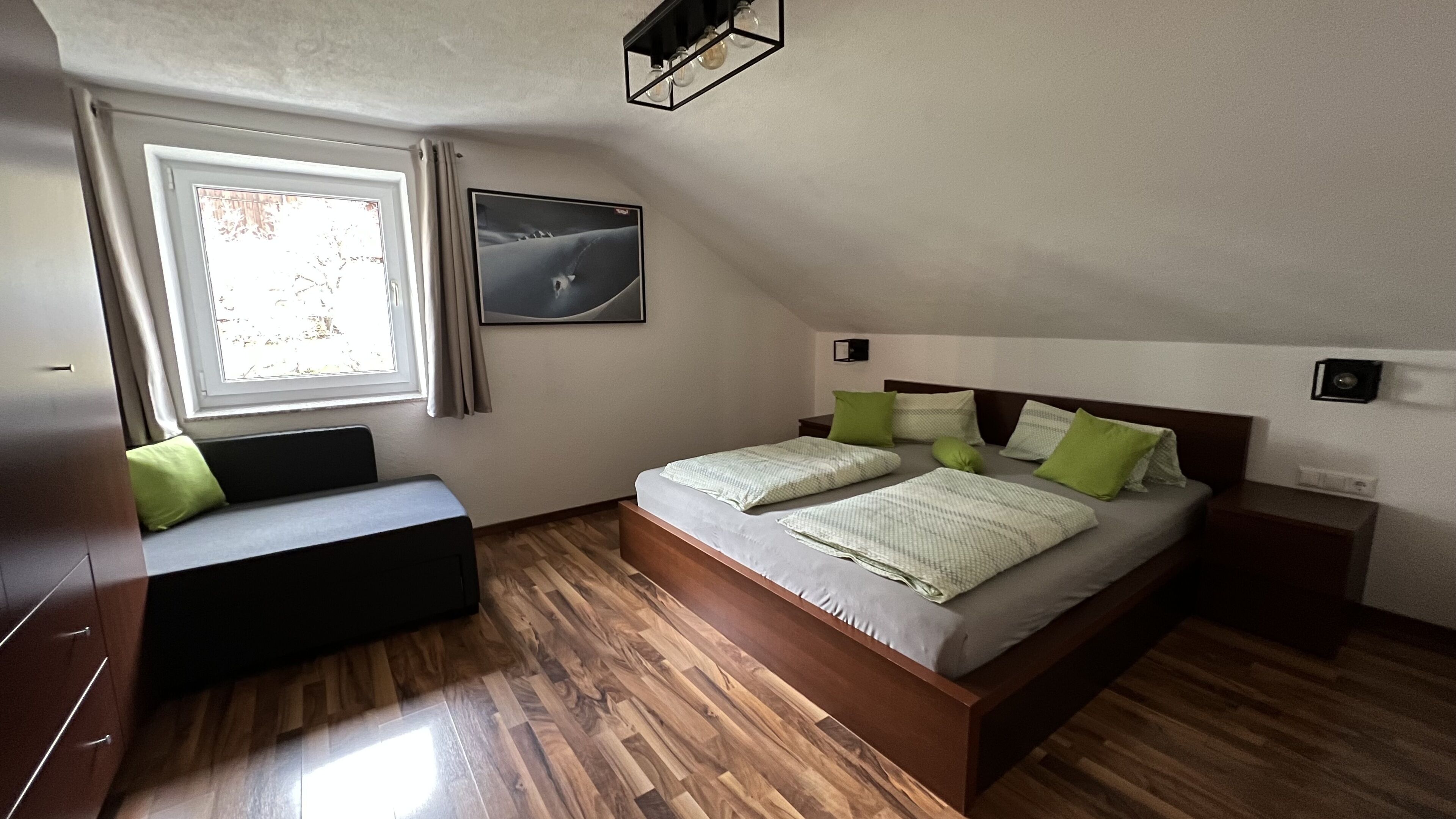 A bedroom with a bed, a bench, a window, and a picture on the wall.