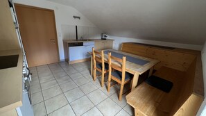 Une cuisine compacte équipée d’un lave-vaisselle, d’un évier et d’une machine à café. On y trouve une table à manger en bois, accompagnée de quatre chaises et d’un banc.