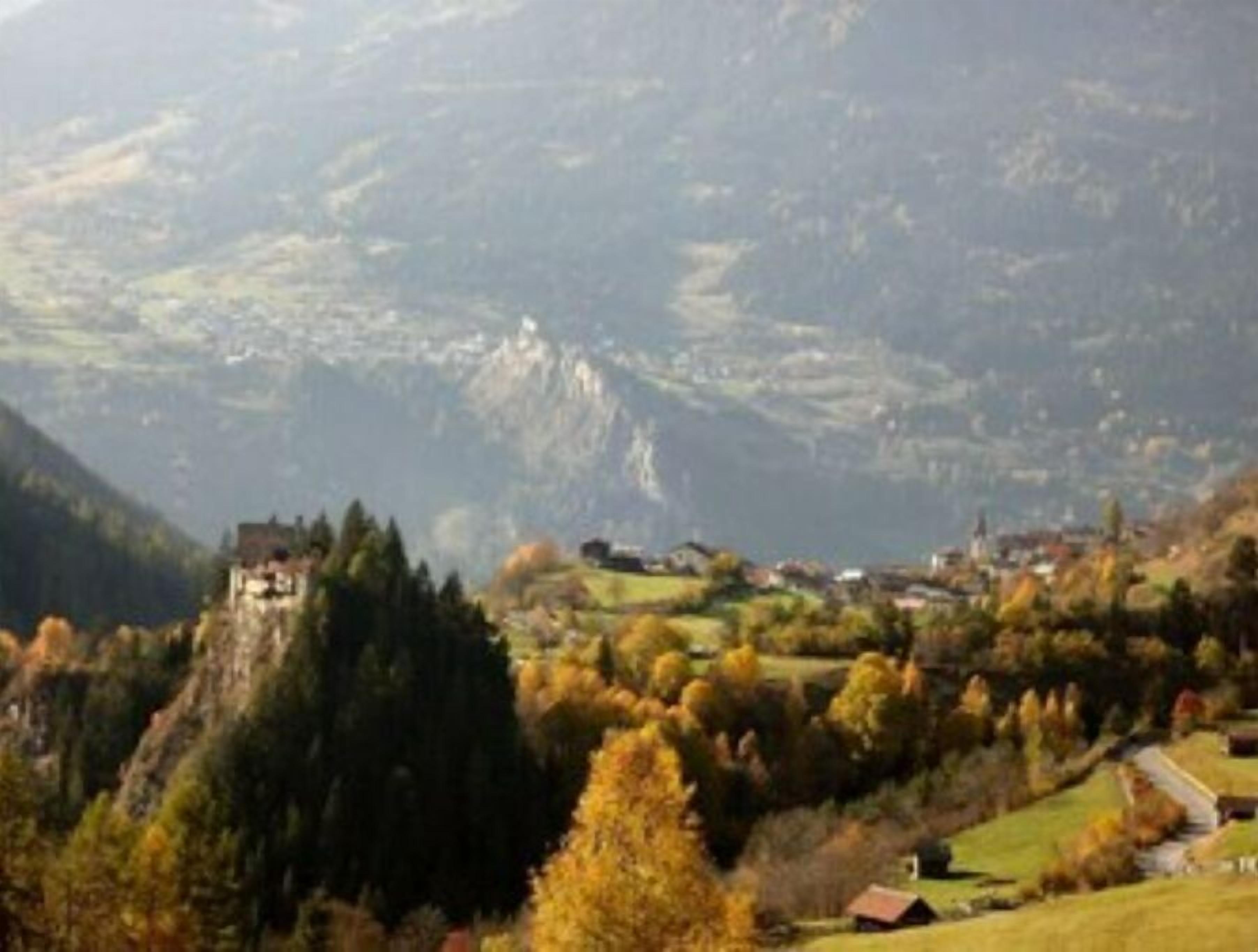 A mountainous landscape with a prominent building on a hill, surrounded by trees and a small village below.