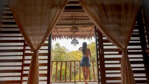 A wooden balcony with a thatched roof and curtains, overlooking a natural landscape. - BioHotel Arara River (Leticia)