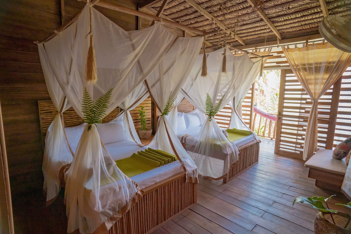 Quarto com quatro camas de madeira, cada uma com dossel e almofadas verdes.