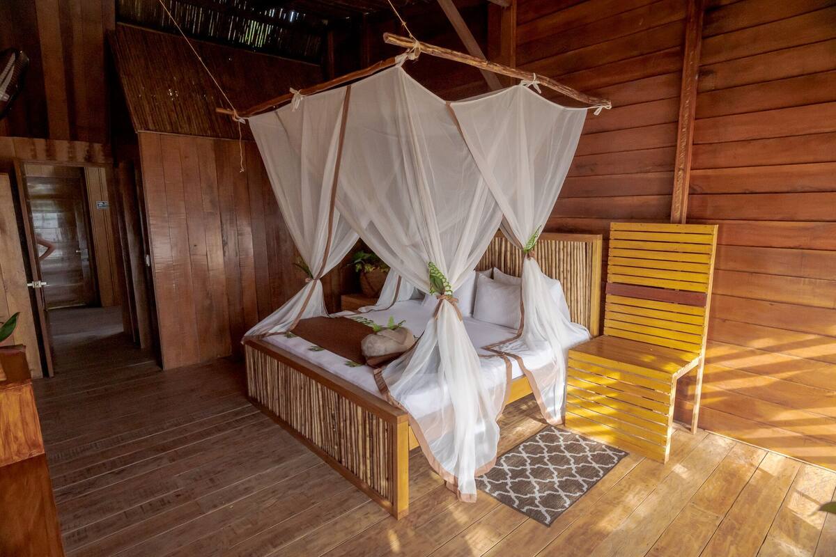 Quarto de madeira com uma cama sob um dossel, um banco de madeira e uma porta.