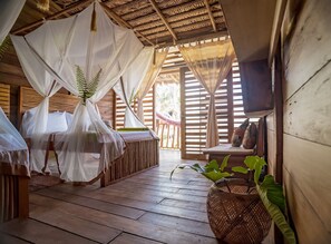 Una habitación con piso de madera, una cama con dosel, una mesita pequeña y una planta grande.