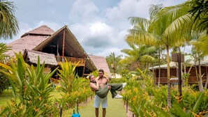 A man standing in a tropical garden with a thatched-roof building in the background. - BioHotel Arara River (Leticia)