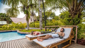 Two lounge chairs by a pool with wooden decking, surrounded by lush greenery and palm trees. - BioHotel Arara River (Leticia)