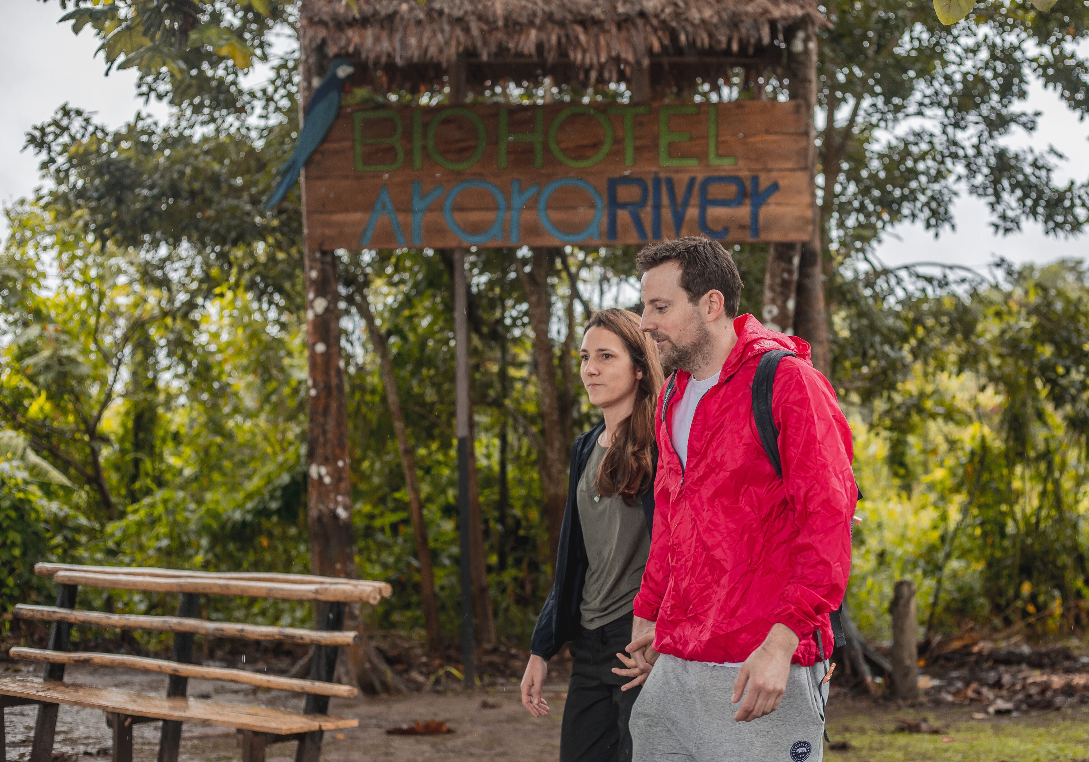 A wooden sign with the text "BIOHOTEL Ayororivey" in a natural setting with trees and a bench.