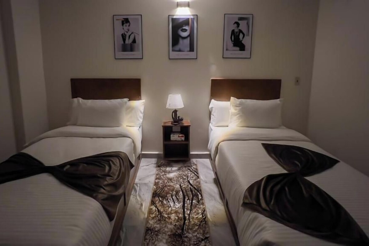 A hotel room with two beds, a nightstand with a lamp, and framed pictures on the wall.