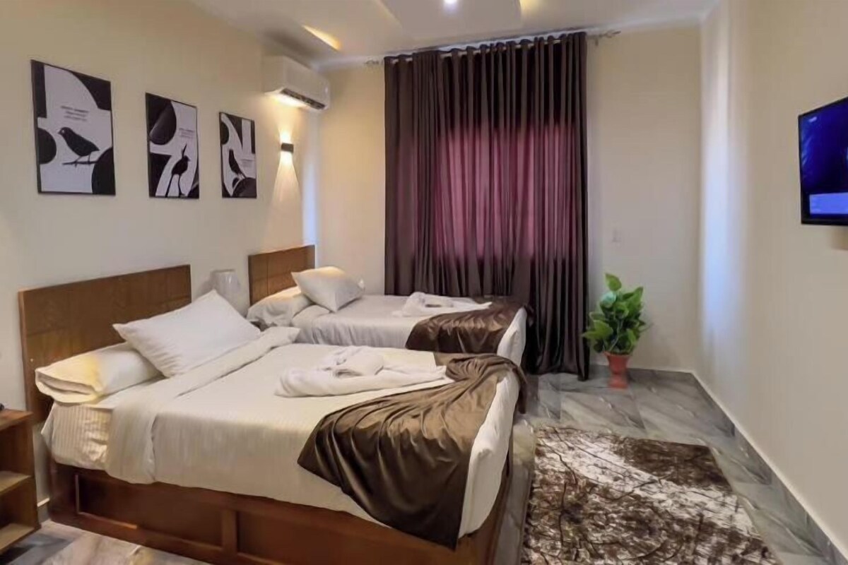 Habitación de hotel con dos camas, un televisor de pantalla plana, una obra de arte en la pared y una planta en maceta.