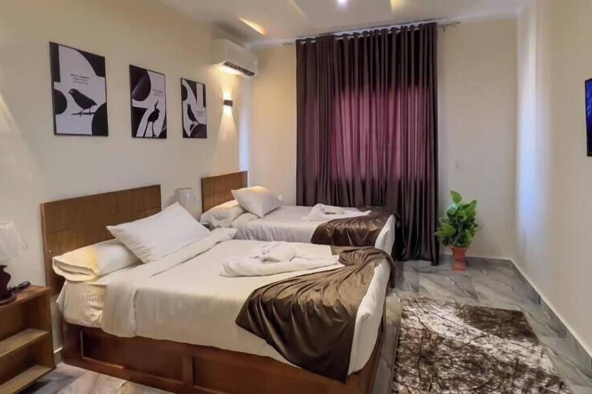 A hotel room with two beds, a flat-screen TV, artwork on the wall, and a potted plant.