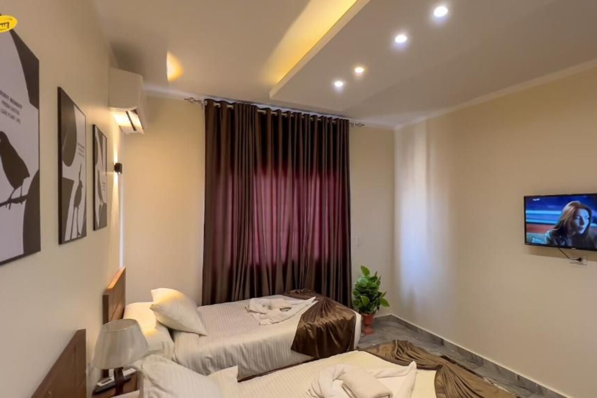 Ein Hotelzimmer mit zwei Betten, einem Fernseher, einer Pflanze und einem Vorhang.