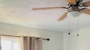 Une chambre avec deux lits, un ventilateur de plafond et une fenêtre avec des rideaux.